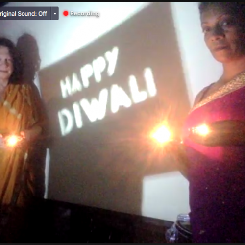 Happy Diwali, A shadow sign saying Happy Diwali is projected on a screen between two people wearing Saris and holding candles